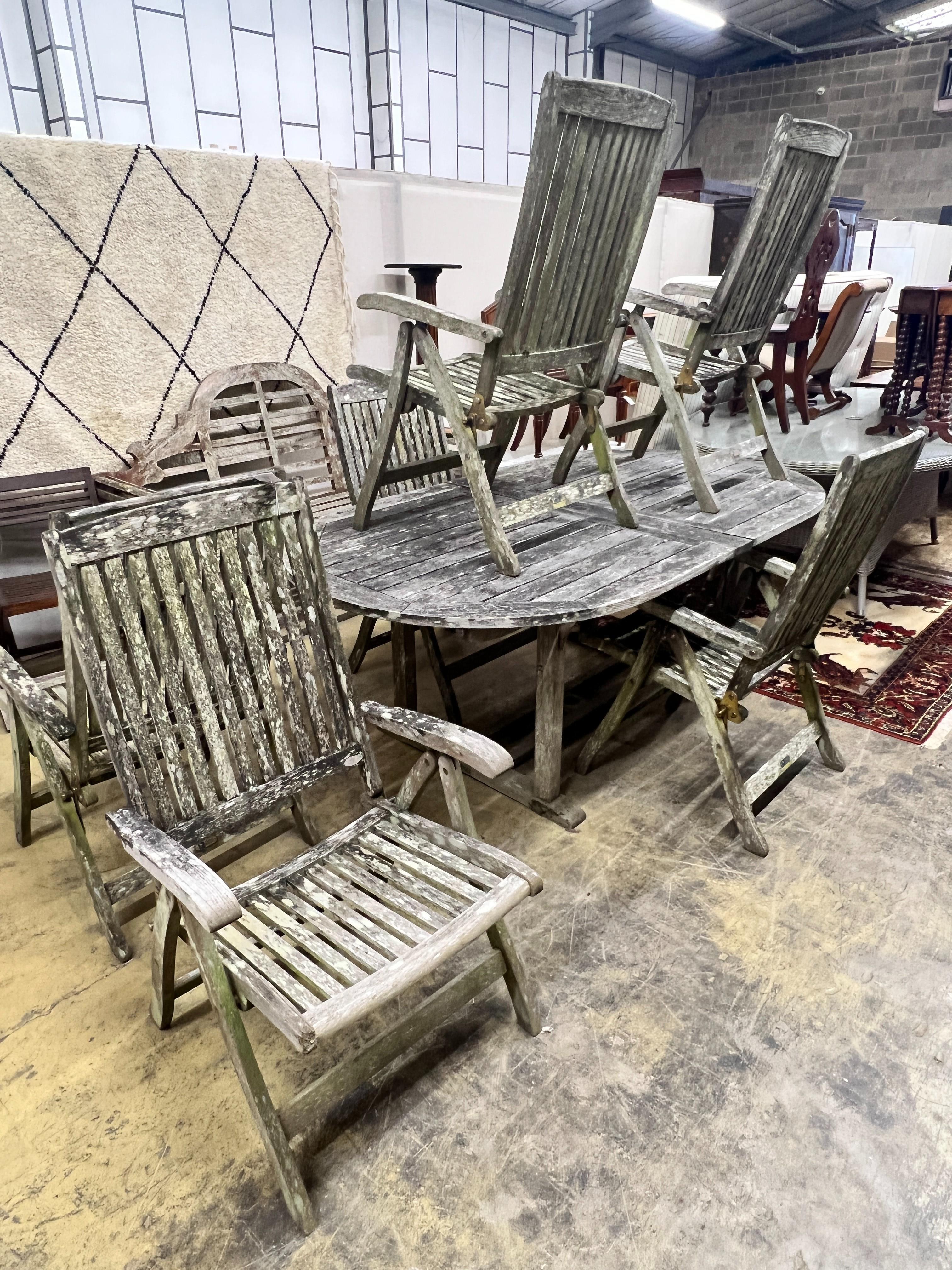 A weathered teak oval extending garden table, extended 250cm, width 109cm, height 73cm, together with six weathered teak folding garden elbow chairs